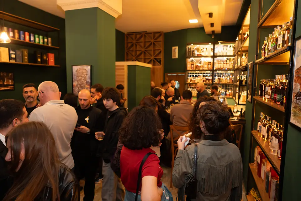 Guests filling the room at BARD Whisky Bar in Tbilisi, with lit whisky shelves along the walls